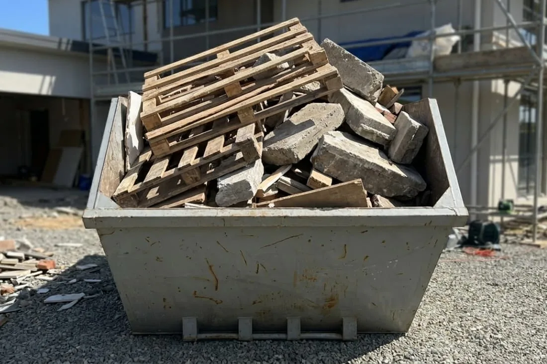 Long term skip hire solutions skip filled with wooden pallets and heavy concrete slabs at an active build site.