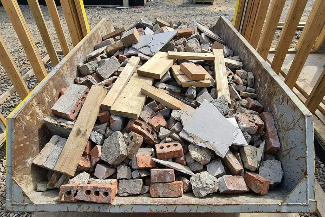 Skip hire for contractors projects mixed bricks, tiles, timber, and rubble filling a builders skip on a work site.