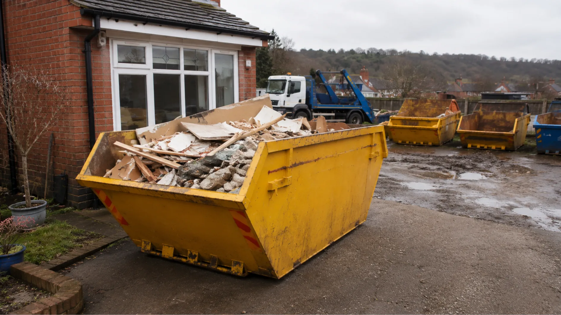 Builders skip filled with renovation waste, with different skip sizes and a delivery truck in the background.